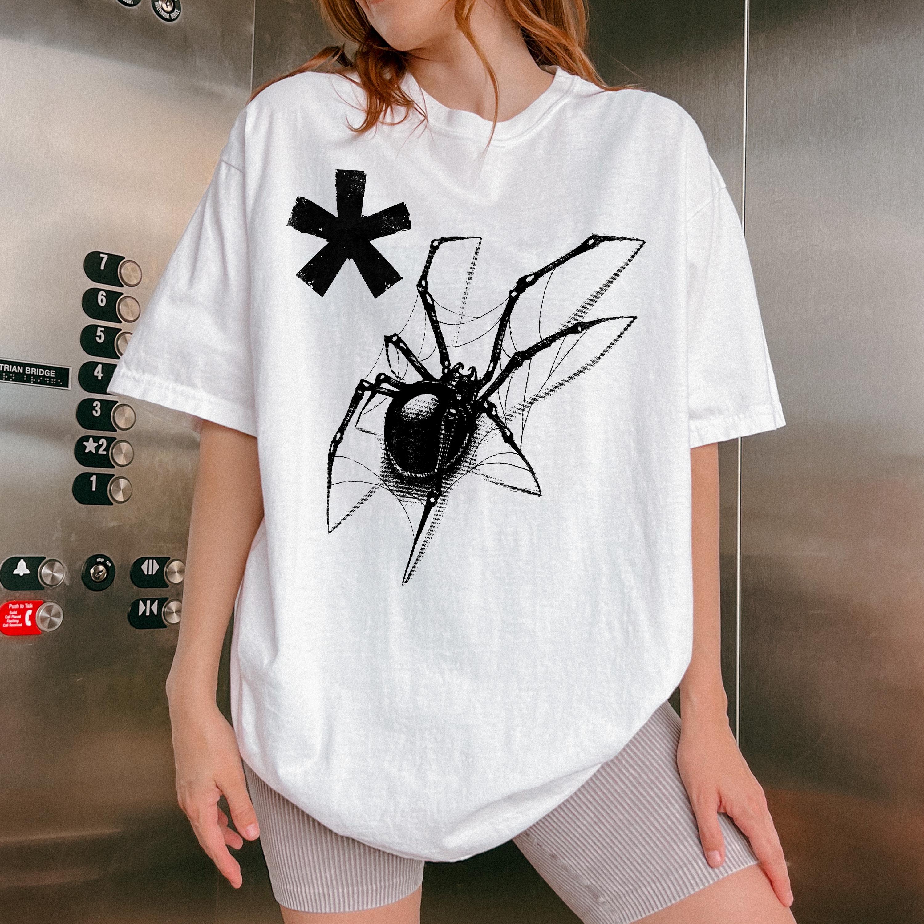 May include: White oversized t-shirt featuring a black spider graphic and a black asterisk. The spider is depicted on a web. The shirt is a relaxed fit and appears to be made of a soft, comfortable material.