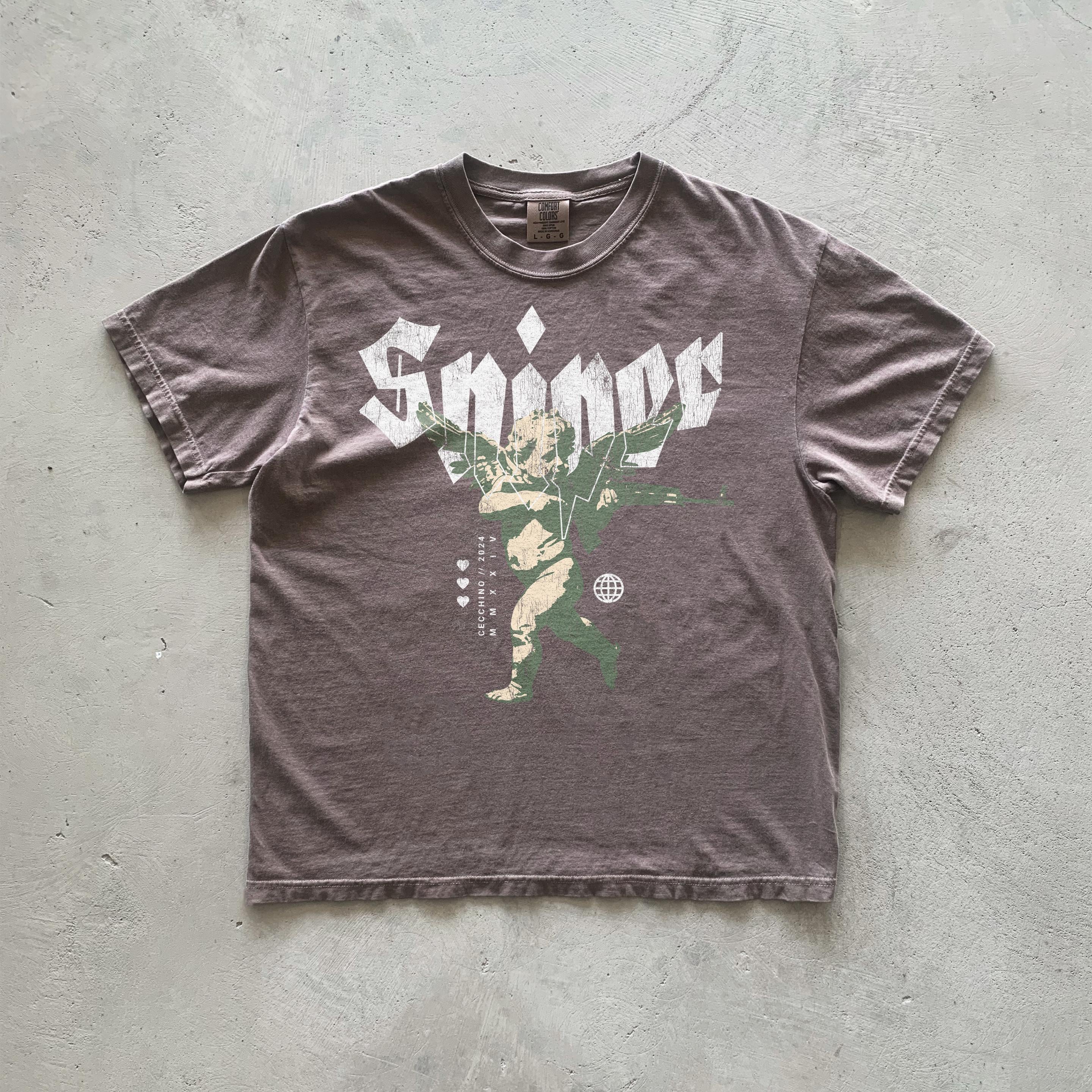 A dark taupe short-sleeved t-shirt features a graphic design of a cherubic figure with wings, holding weapons, superimposed on the word 'Sniper' in stylized lettering.