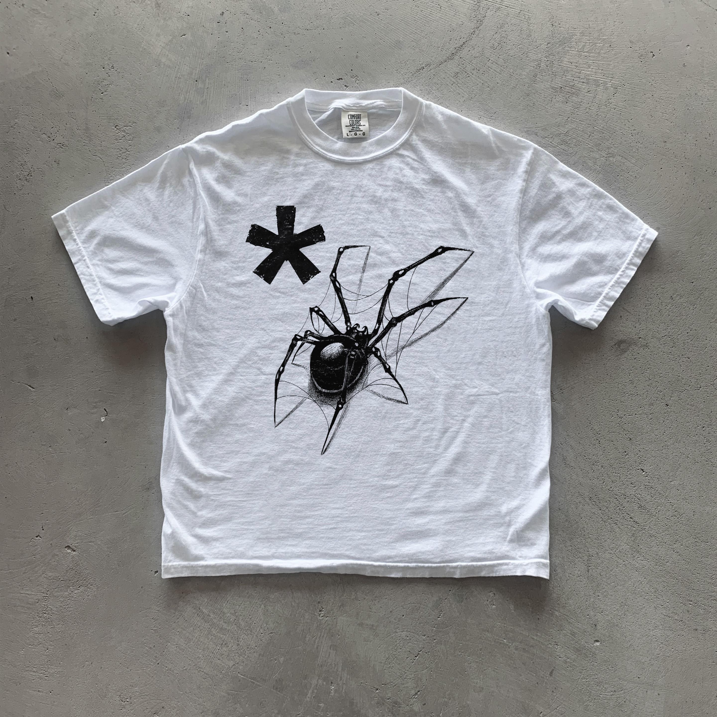 May include: White t-shirt featuring a black spider graphic and a black asterisk. The spider is depicted in detail, with its legs spread out on a web. The asterisk is located above the spider. The t-shirt is a classic crew neck style, and appears to be made of a soft, lightweight cotton material.