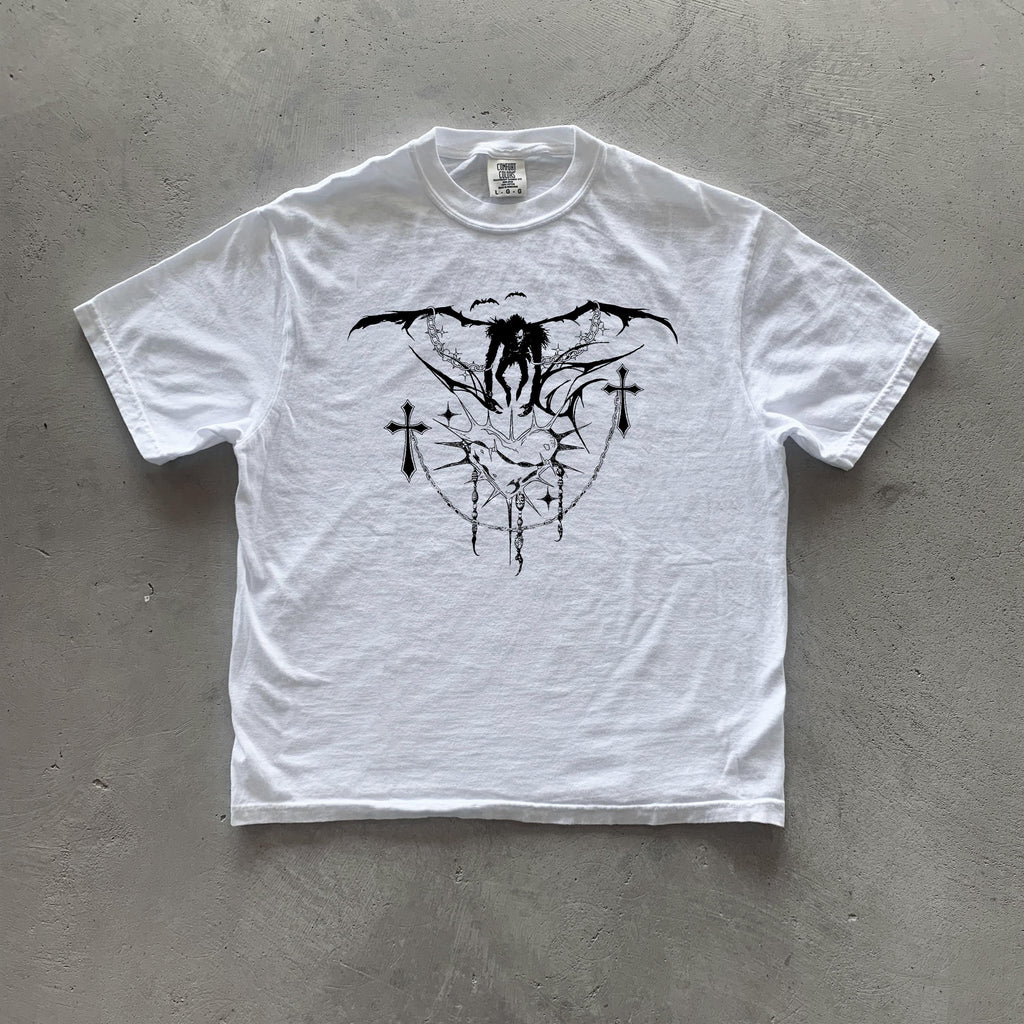 May include: White t-shirt with a black graphic print of a winged figure with crosses and a heart design.