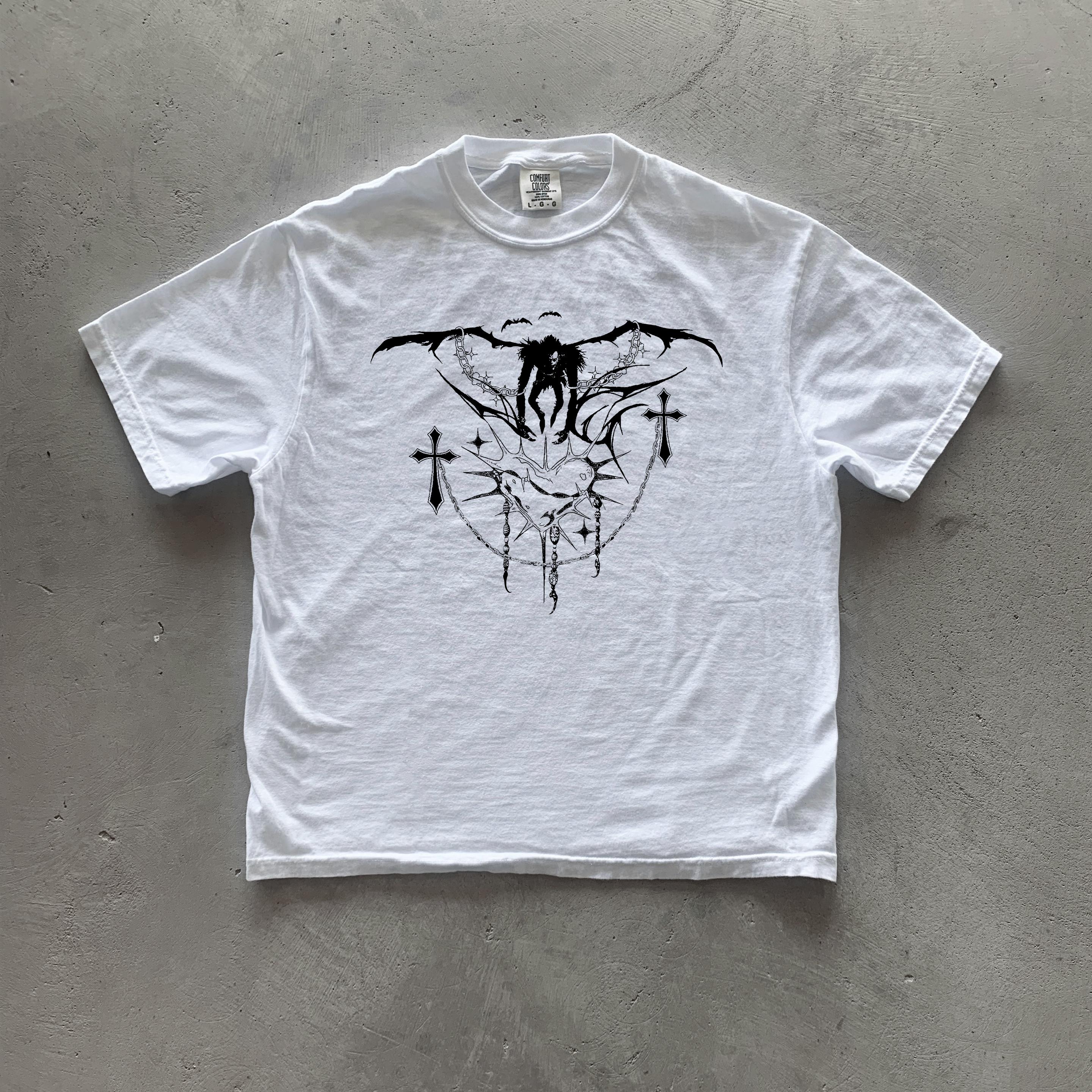 May include: White t-shirt with a black graphic print of a winged figure with crosses and a heart design.
