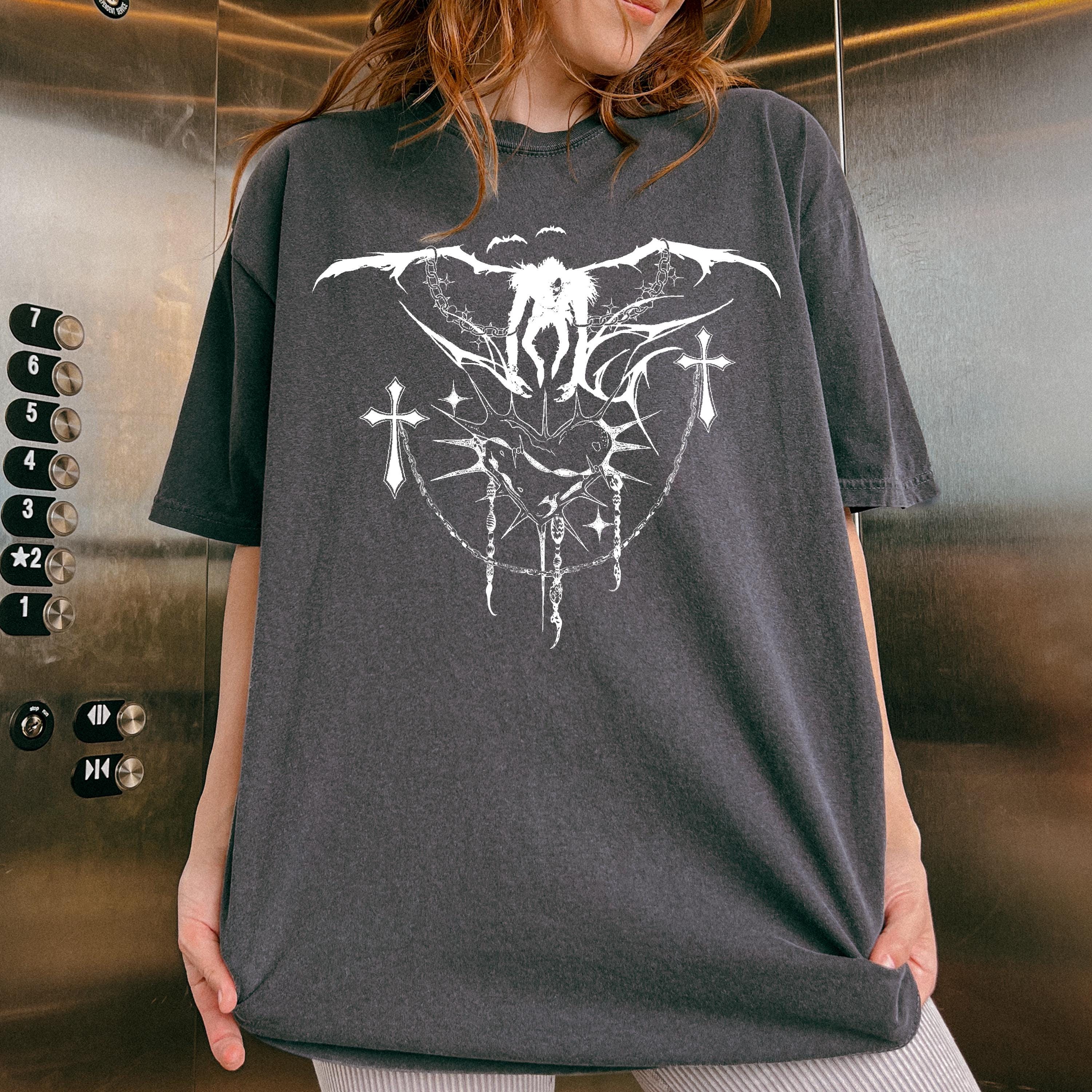 May include: A black t-shirt with a white graphic print of a winged figure with a halo and a cross. The graphic is surrounded by a chain link design with thorns and stars.